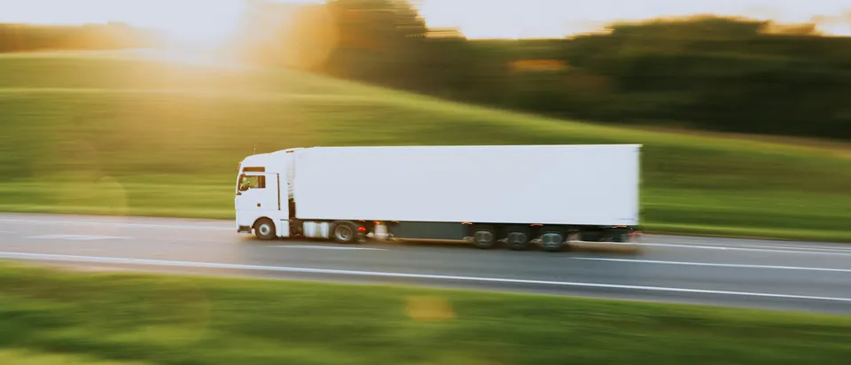 Witte vrachtwagen zonder opdruk op een snelweg bij zonsondergang