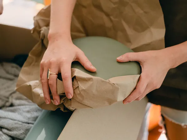 Handen pakken een breekbaar voorwerp in bruin inpakpapier
